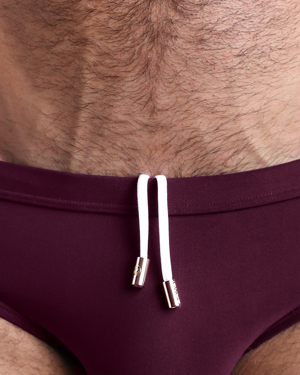 Close-up view of men’s summer swimwear by BANG! clothing brand, showing white cord with custom branded golden cord ends, and matching custom eyelet trims in gold.