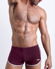 Frontal view of a sexy male model wearing men’s swimsuit in dark purple red color by the Bang! Menswear brand from Miami.