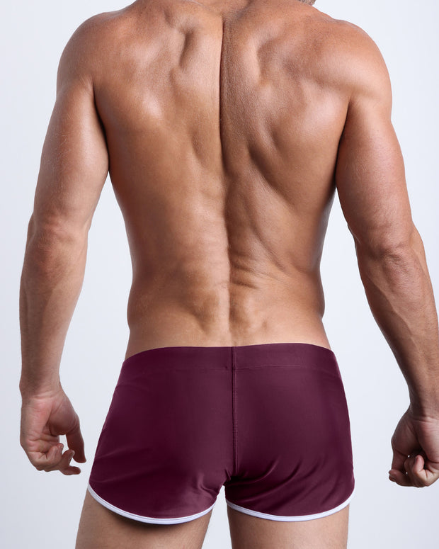 Back view of a male model wearing men’s swim shorts in dark wine red color by the Bang! Clothes brand of men&