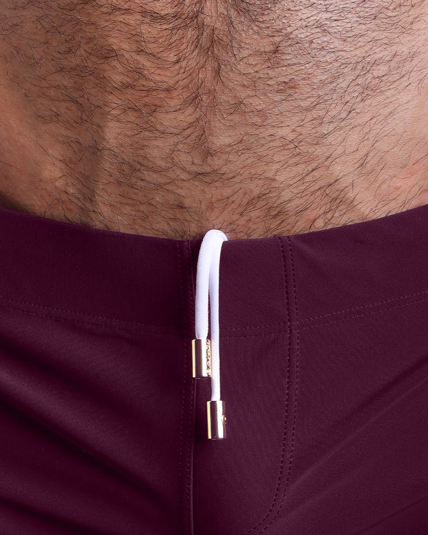 Close-up view of men’s summer beach shorts by BANG! clothing brand, showing white cord with custom branded golden cord ends, and matching custom eyelet trims in gold.