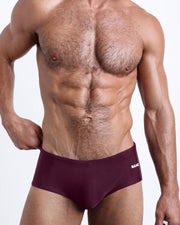 Frontal view of a sexy male model wearing men’s swimsuit in VERY BERRY a dark burgundy color color by the Bang! Menswear brand from Miami.