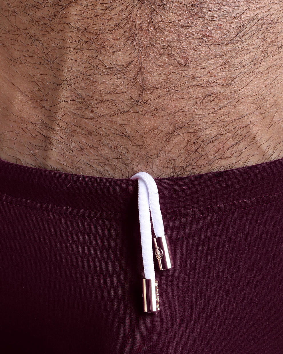 Close-up view of the VERY BERRY Swim Sunga mens swimsuit a dark red color with white internal drawstring cord showing custom branded golden buttons by BANG! clothing brand.