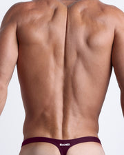 Back view of a male model wearing men’s swim thongs in dark red purple color by the Bang! Clothes brand of men's beachwear.