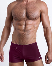 Frontal view of a sexy male model wearing men’s swimsuit with mini pockets in burgundy red color by the Bang! Menswear brand from Miami.