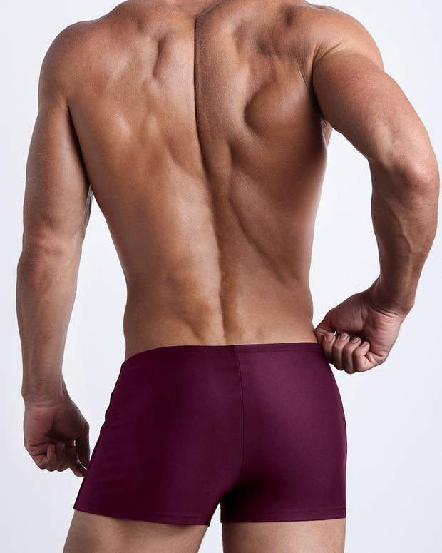 Back view of a male model wearing the VERY BERRY men’s swim trunks in a solid wine red color by the Bang! Clothes brand of men&