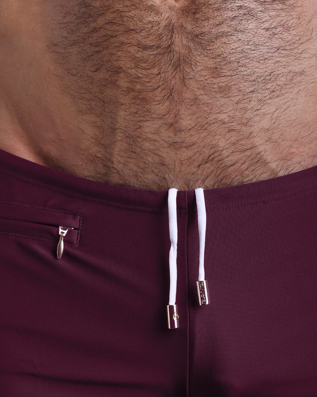 Close-up view of the VERY BERRY Swim Trunks mens swimsuit a dark red color with white internal drawstring cord showing custom branded golden buttons by BANG! clothing brand.