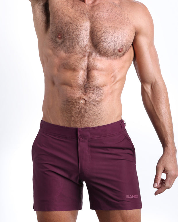 Frontal view of a sexy male model wearing the men’s VERY BERRY beach tailored shorts in burgundy dark red by the Bang! Menswear brand from Miami.