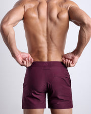 Back view of a male model wearing the VERY BERRY Tailored Shorts men’s beach shorts in a dark wine color by the Bang! Clothes brand of men's beachwear.