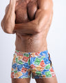 Front view of model wearing the VIA POSTAL men’swim bottoms in white with colorful Miami pop art postage stamps designed by the Bang! Clothes brand of men's beachwear from Miami.