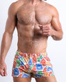 Frontal view of model wearing the VIA POSTAL men’s square leg swim trunks in white with colorful Miami pop art postage stamps print by the Bang! brand of men's beachwear from Miami.