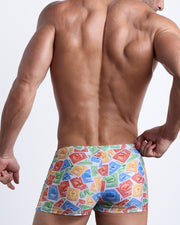 Back view of a Male model wearing swim trunks for men featuring red, green, yellow Miami Postage stamps by the Bang! Clothes brand of men's beachwear.