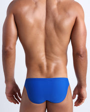 Back view of a male model wearing men’s swim mini-brief in cobalt color by the Bang! Clothes brand of men's beachwear.