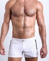 Frontal view of male model wearing the WHITE PARTY men’s beach shorts in a white color by the Bang! brand of men's beachwear from Miami.