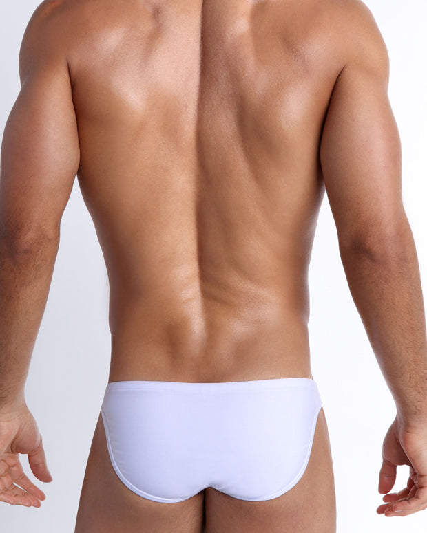 Back view of a male model wearing men’s swim mini-brief in smooth white color by the Bang! Clothes brand of men&