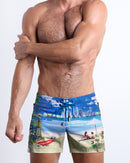 Frontal view of model wearing the WISH YOU WERE HERE men’s mini swimming shorts in sky blue color featuring the Miami Beach skyline by the Bang! menswear brand.