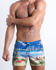 Frontal view of model wearing the WISH YOU WERE HERE men’s mini swimming shorts in sky blue color featuring the Miami Beach skyline by the Bang! menswear brand.