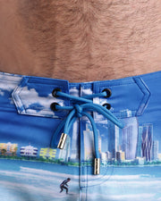 Close-up view of men’s summer beach shorts by BANG! clothing brand, showing blue cord with custom branded golden cord ends, and matching custom eyelet trims in gold.