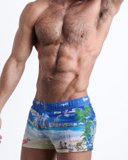 Side view of an in-shape male model wearing WISH YOU WERE HERE mini shorts for men featuring a colorful Miami inspired artwork made by the Miami-based Bang! brand of men's beachwear.