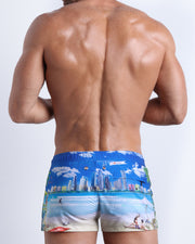 Back side view of sexy male model wearing men's WISH YOU WERE HERE swimwear speedo shorts in white with a beach inspired art made by Miami based Bang brand of men's beachwear.