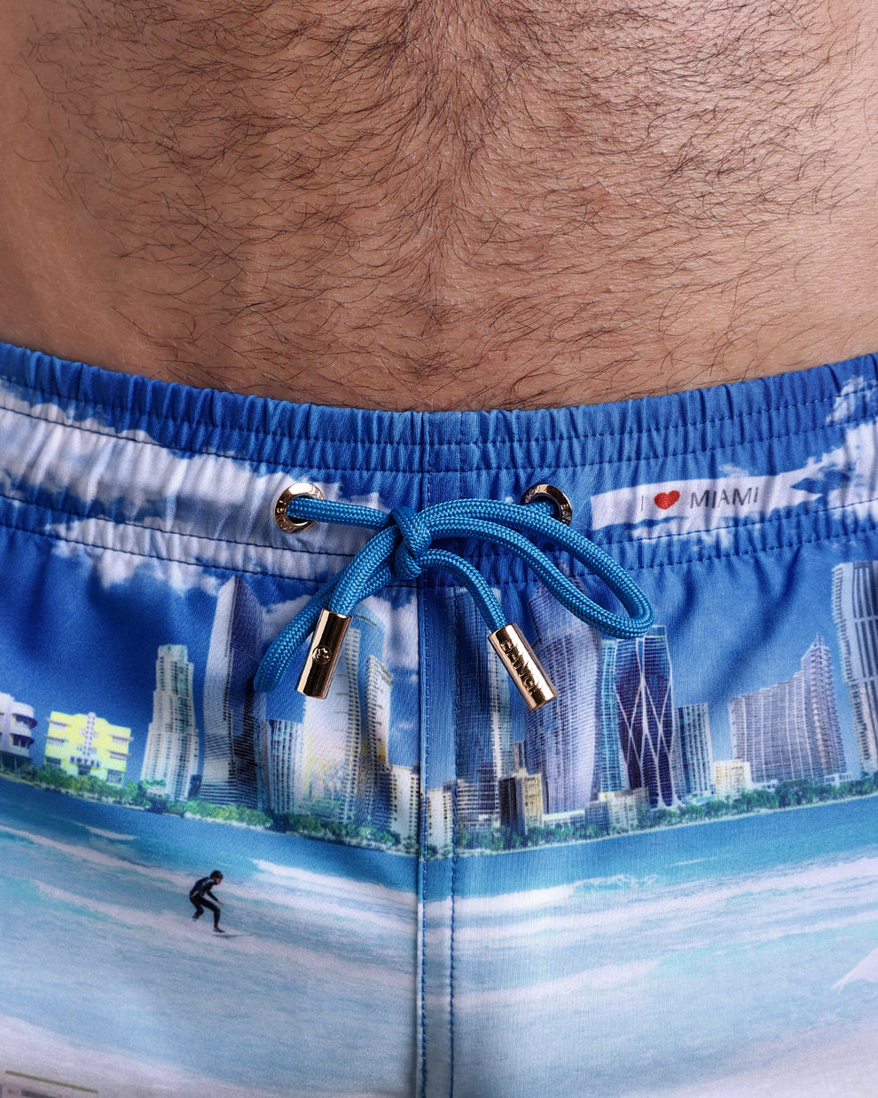 Close-up view of the WISH YOU WERE HERE men’s summer shorts, showing blue cord with custom branded golden cord ends, and matching custom eyelet trims in gold.