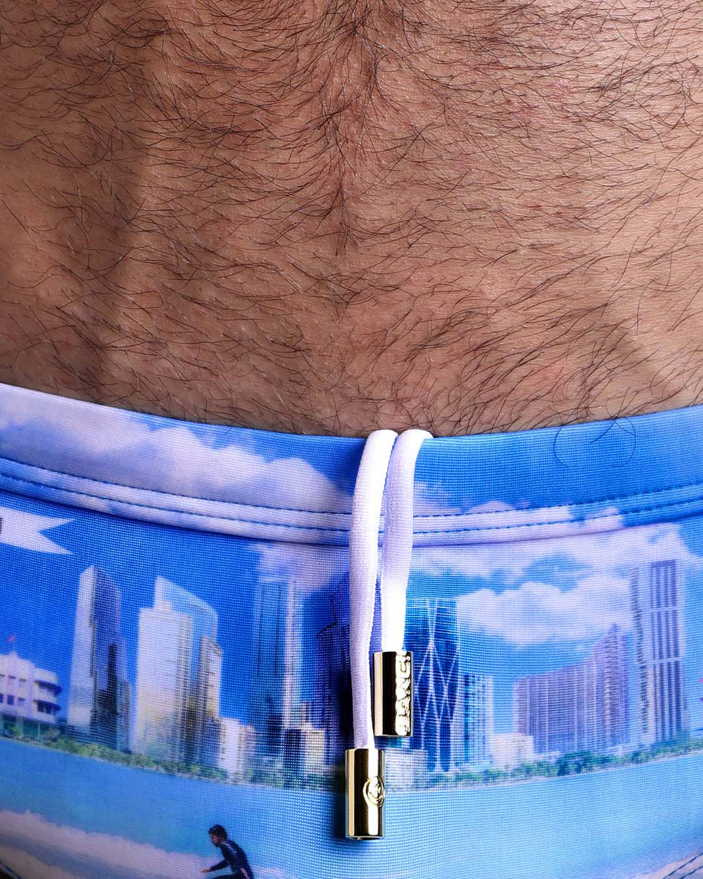 Close-up view of the WISH YOU WERE HERE men’s drawstring briefs showing white cord with custom branded golden cord ends, and matching custom eyelet trims in gold.