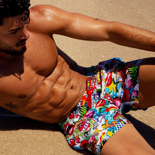 front view of a sexy male model wearing BANG Miami yeah yeah show shorts unique prints in a beach setting summer body ripped
