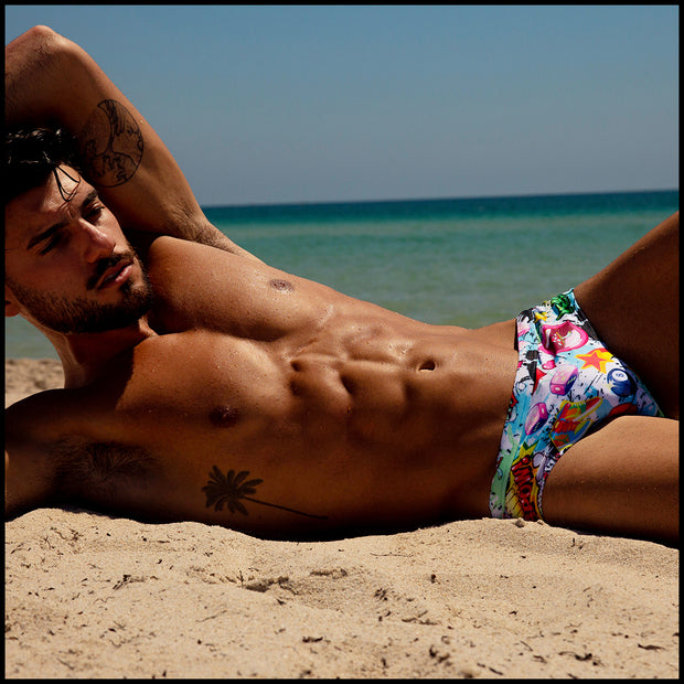 Front view of a sexy male model wearing BANG Miami premium Swim Brief in yeah yeah print unique comics red green blue white yellow