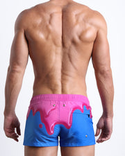 Back side view of sexy male model wearing men's YOU MELT ME swimwear speedo shorts featuring magenta pink melting ice cream print made by Miami based Bang brand of men's beachwear.