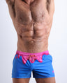 Front view of model wearing the YOU MELT ME men’s beach shorts in a bright blue color featuring pink melting ice cream print by the Bang! Clothes brand of men's beachwear from Miami.