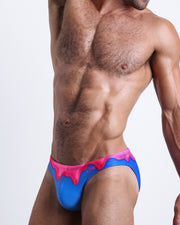 Side view of muscular male model wearing YOU MELT ME Summer swimsuit for the beach in blue and hot pink melting ice cream print by BANG! Miami.