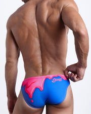 Back view of a model wearing YOU MELT ME men’s beach mini-brief featuring magenta pink melting ice cream print made by the Bang! Miami official brand of men's swimwear.