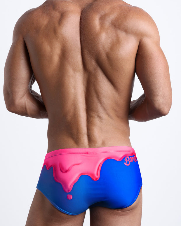 Back view of a Male model wearing Brazilian Beach Sunga Swimsuit for men in blue and hot pink strawberry melting ice cream print by the Bang! Clothes brand of men&