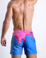 Back view of male model wearing the YOU MELT ME beach trunks for men by BANG! Miami in blue and hot pink melting ice cream theme.