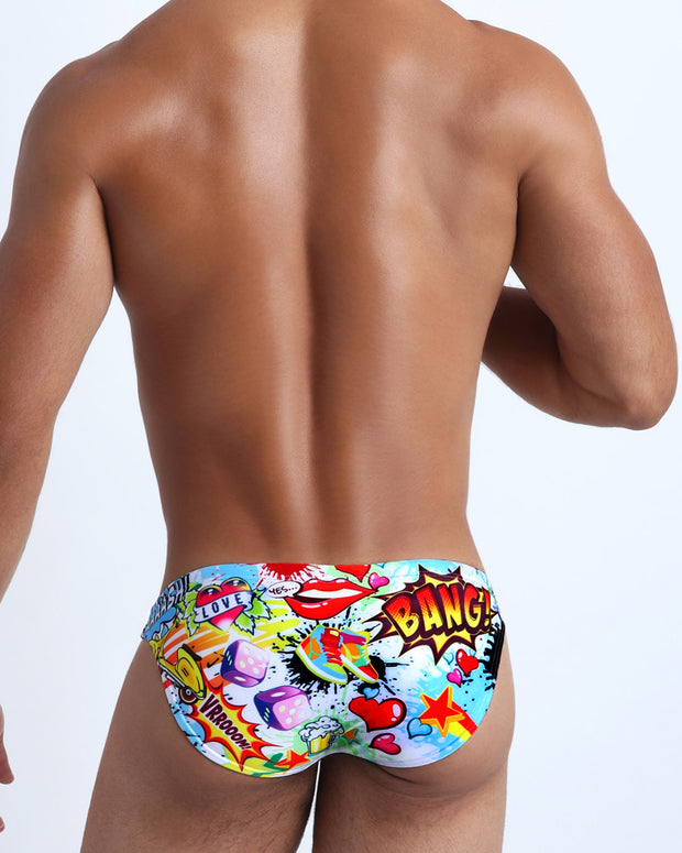 Back view of a male model wearing Yeah Yeah premium quality bikini-style bathing suit in a graffiti style bold print.
